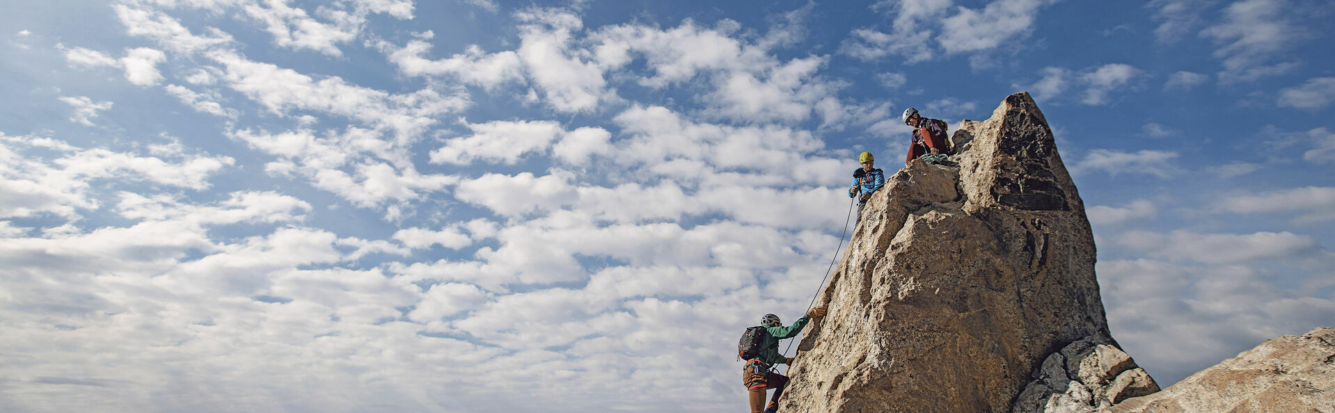 Three rock climbers each the summit of a mountain in Tetons, Wyo